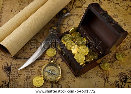 Old brass compass lying on a very old map with treasure chest full of golden coins