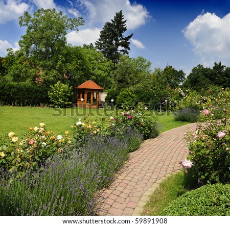 Beautiful garden with blooming roses, brick path and a small gazebo