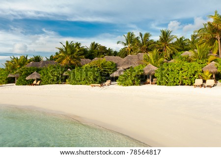Beautiful tropical paradise in Maldives with coco palms hanging over the white beach, cozy bungalows and turquoise sea