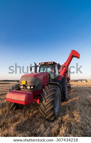 Agriculture tractor and tow trailer waiting to be filled at grain campaign at sunset on a stubble field