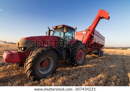 Agriculture tractor and tow trailer waiting to be filled at grain campaign at sunset on a stubble field
