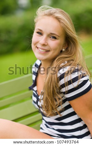 Young smiling girl sitting on the park chair with very narrow depth of field and focus on the eyes