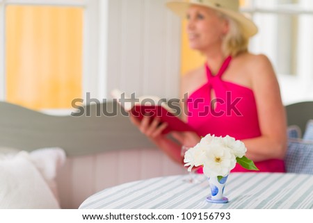Lady reads a book on the veranda, reposeful atmosphere, vertical format, narrow focus on flower, lady looks outside