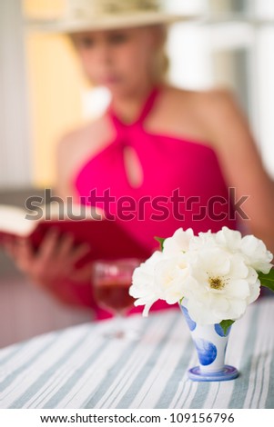 Lady reads a book on the veranda, reposeful atmosphere, vertical format, narrow focus on flower