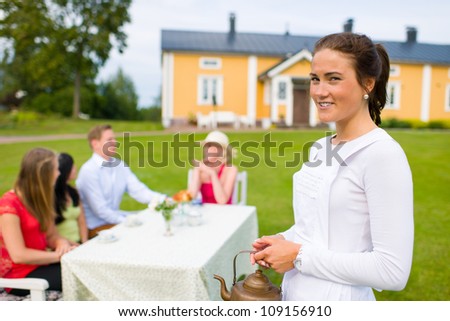 Smiling waitress standing front of customer group, who sitting on coffee table