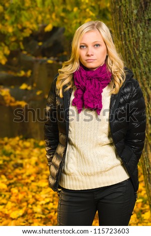 Beautiful girl poses on a park, autumn color leaves on the background, vertical format