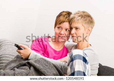 Happy lesbian couple watching a television on the sofa, close-up