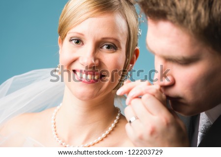 Happy smiling bride, groom kissing hand of the bride, blue background, vertical format, horizon format