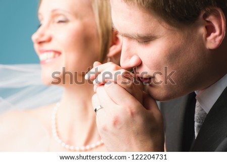 Groom kissing hand of the bride, bride has eyes closed, blue background