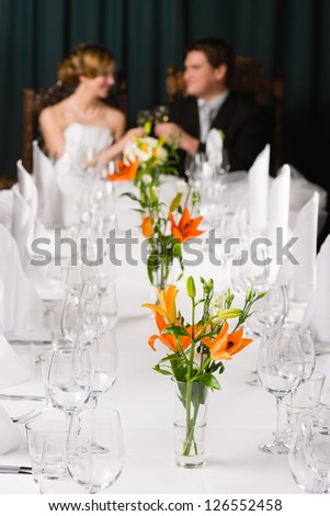 Table setting, focus on foreground flower, bride and groom toasting on background