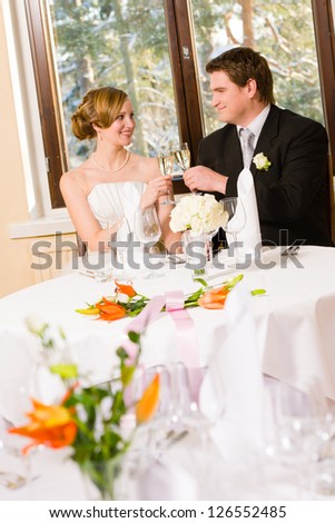 Happy bride and groom toasting champagne, table setting and flowers foreground
