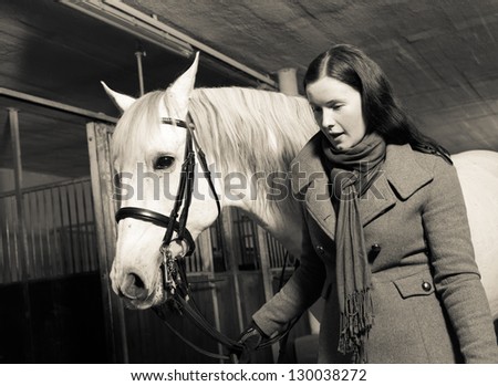 Woman leads white horse inside a barn, horizon format
