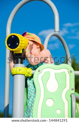Young girl use binoculars on jungle gym, sunny day