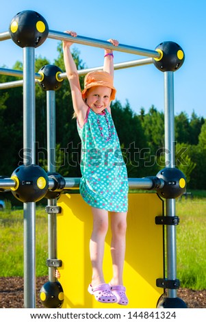 Young girl hangs on the jungle gym, sunny day