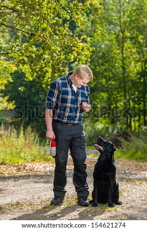 Dog owner trains his labrador retriever on outdoor, dog sits on alongside, vertical format