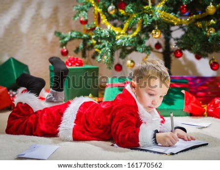 Adorable 5 year old boy writes to Santa Claus, Christmas tree on background