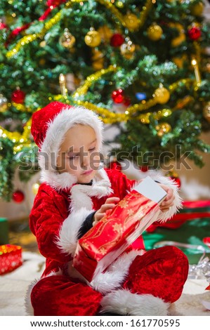 Boy opens a Christmas gift, Christmas tree and gifts on background