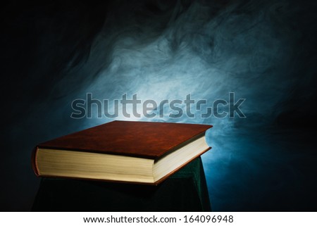 Unopened big book and smoke, dark background, horizon format
