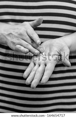 Mature woman spread out skincare cream to her hand, vertical format black and white image