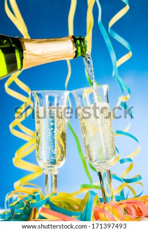 A bottle and two glass of sparkling wine, streamers and blue background