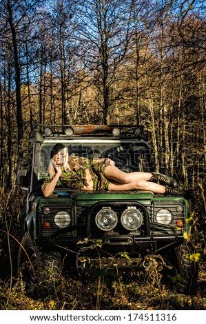 Beautiful girl on camouflage outfit lying top of the off-road vehicle bonnet