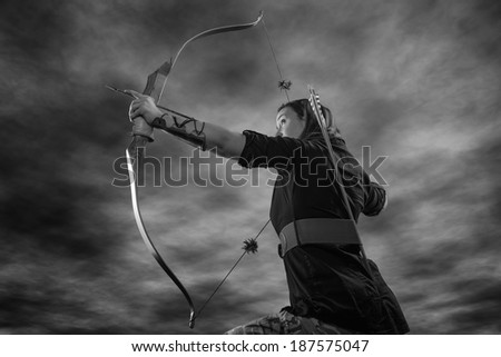 Beautiful archery woman aiming, sky on background, black and white image