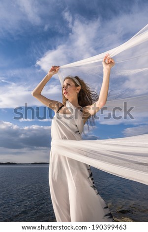 Portrait of young beautiful woman with waving fabric in her arms on wind