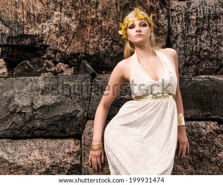 Beautiful makeup girl wearing white tunic and an antique jewels, rocky wall on background