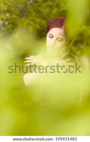 Close-up - beautiful makeup girl wearing black tunic and an antique jewels, green leaves around