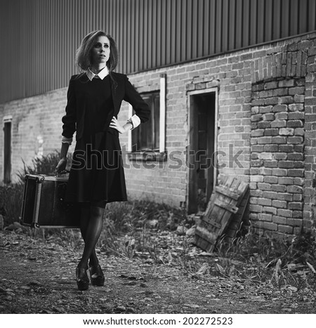 Fashionable young woman with her suitcase, old rural scene, black and white image