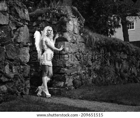 Sexy woman wearing white angel costume and wings, stone wall