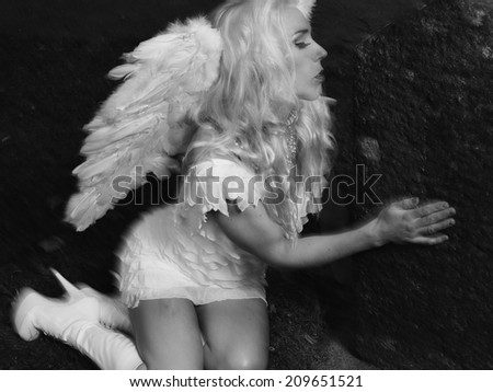 Sexy woman wearing white angel costume and wings, she leans to the tombstone - motion blurring, combination of natural and flash lights