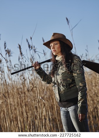 Waterfowl hunting, female hunter carry a shotgun, reeds and blue sky on background
