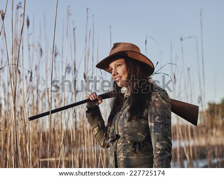 Waterfowl hunting, female hunter carry a shotgun, reeds and blue sky on background - close up and horizon format