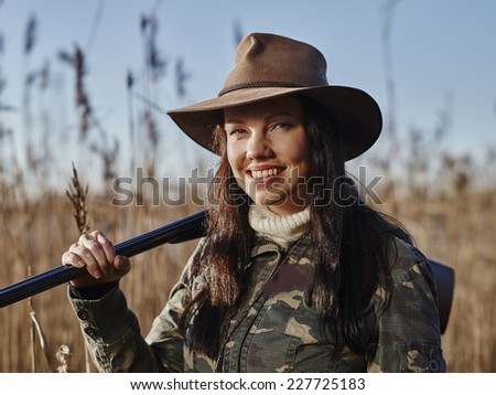 Waterfowl hunting, smiling female hunter carry a shotgun and she looks toward the camera, reeds and blue sky on background