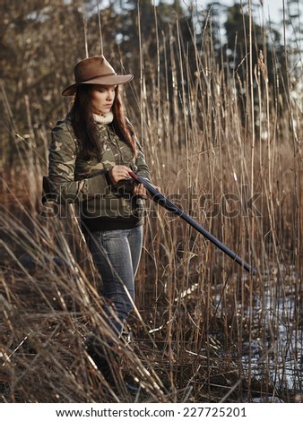 Waterfowl hunting, the female hunter loading the side by side shotgun, shore and reeds on background