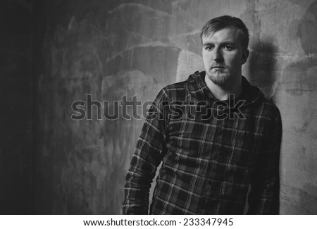 Handsome young man wearing a checked shirt and he lean against the the concrete wall - black and white image