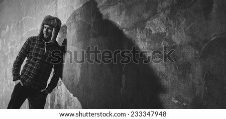 Handsome young man wearing a checked shirt and fur hat and he lean against the the concrete wall - black and white image