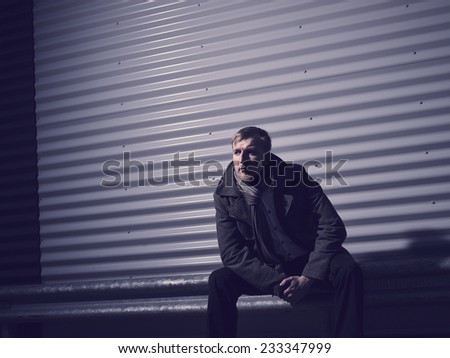 Fashionable young man wearing a warm overcoat, corrugated iron wall on background - cross processed image