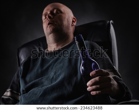 Middle aged man sleeps on an armchair and he holding a wine bottle, horizon format