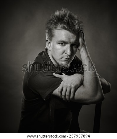 Portrait, handsome young man sits in the studio - black and white image, dark background