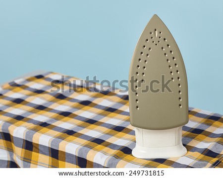 Close up, a iron and checkered shirt on the ironing board, light blue background