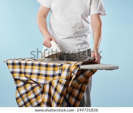 A man, a iron and checkered shirt on the ironing board, light blue background