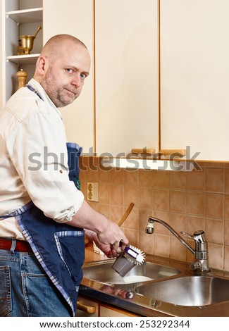 Homeworks, serious man washes dishes by hand and he looks towards to camera