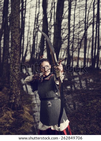 Medieval archer woman, she wearing a chainmail and use a bow and arrow, gloomy forest, cross-processed image.
