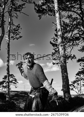Medieval viking warrior wearing chainmail and he has the sword, north nature on background, black and white image