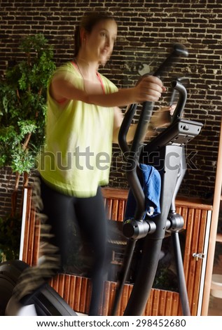 Young woman takes care of his health and she use elliptical trainer, intentional motion blur and narrow field of depth