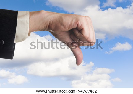 Mans hand, thumbs pointing down, cloudy sky background.