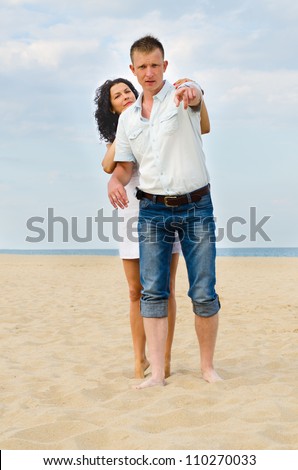 Attractive young couple on a beach with the man pointing out something to his wife who is hugging him from behind