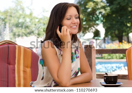 Woman sitting in her garden at a table with a cup  coffee chatting on a mobile phone